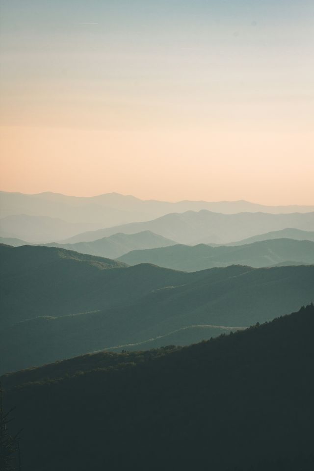 Layered misty mountain ridges under a soft pale sky